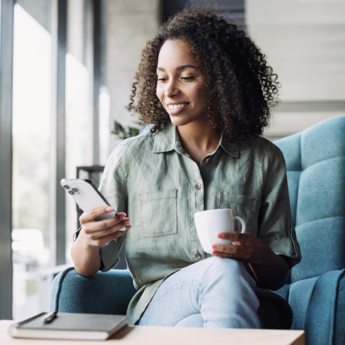 A woman holds a coffee cup and her iPhone.
